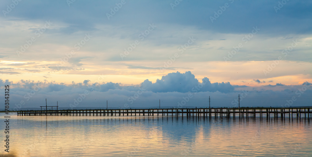 Obraz premium The sky is cloudy and the water is calm with a pier in the mid-ground