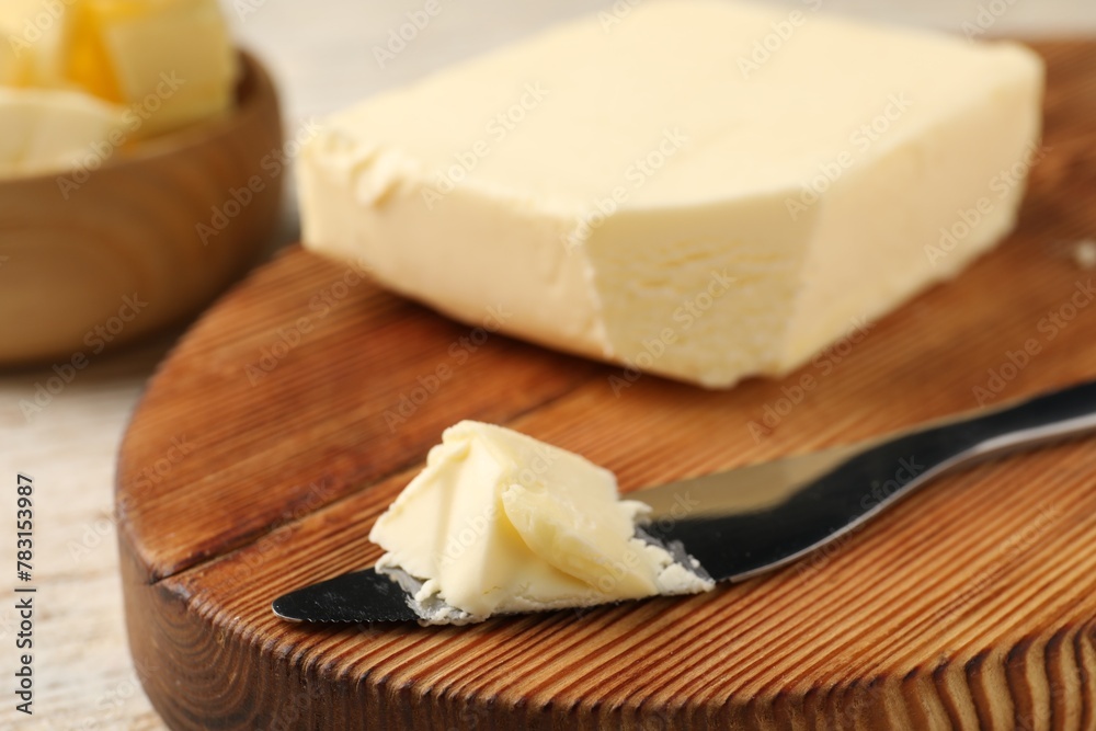 Tasty butter and knife on light wooden table, closeup