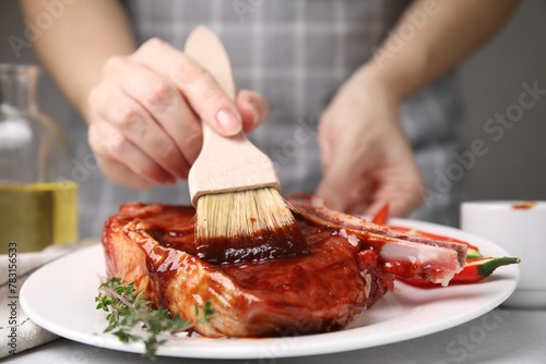 Slika na platnu Woman spreading marinade onto raw meat with basting brush at table, closeup