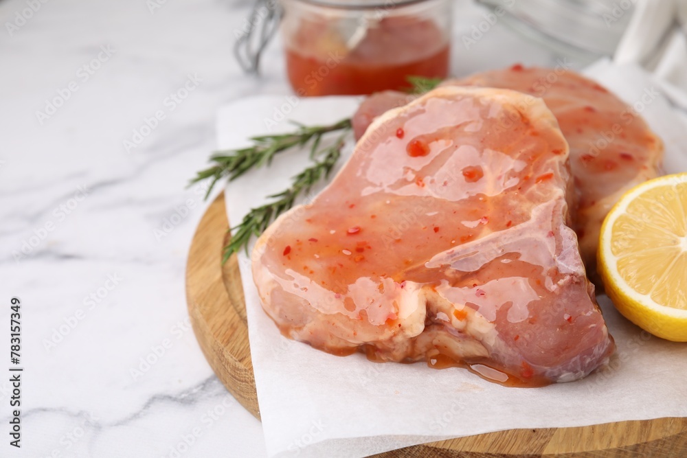 Board with raw marinated meat, lemon and rosemary on white marble table, closeup. Space for text Board with raw marinated meat, lemon and rosemary on white marble table, closeup. Space for text