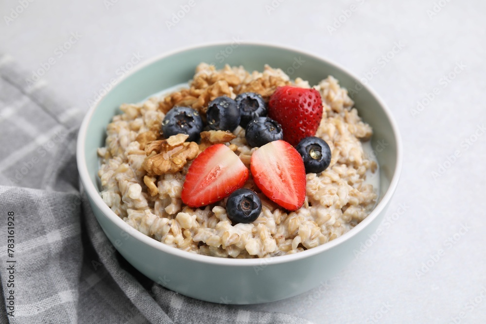 Tasty oatmeal with strawberries, blueberries and walnuts in bowl on grey table Tasty oatmeal with strawberries, blueberries and walnuts in bowl on grey table