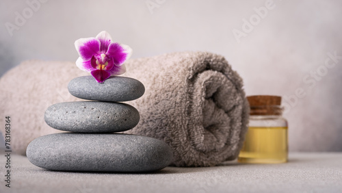 Spa still life with smooth pebbles, a rolled gray towel, and a vibrant purple orchid