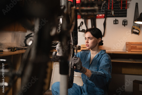 Beautiful brunette girl worker crouching and repairing bicycle. Authentic bike workshop interior.