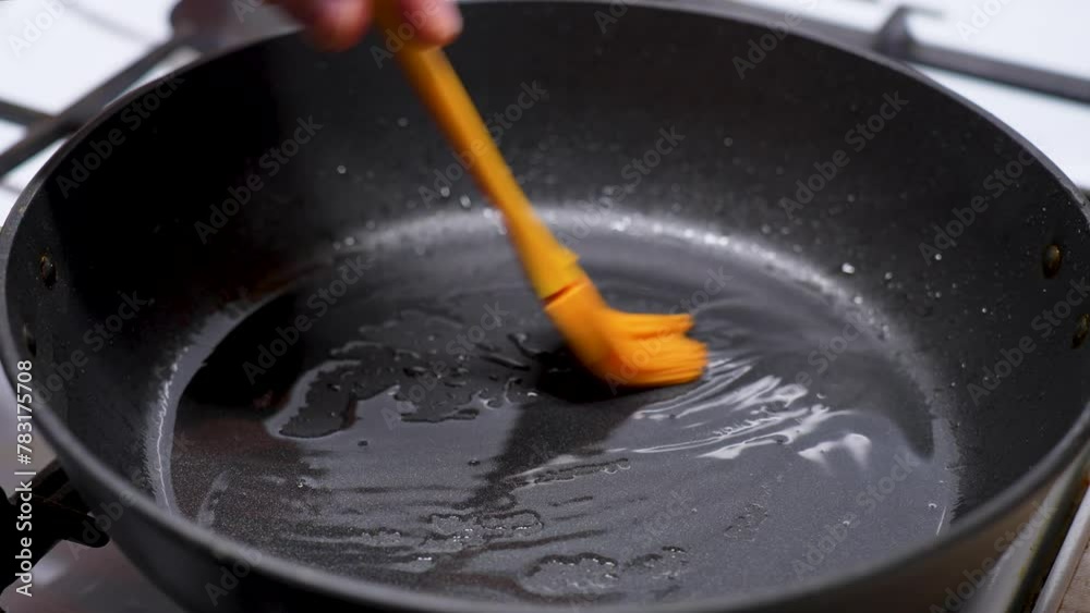 Cooking on frying pan process. Man hands applying sunflower oil with silicone brush Cooking on frying pan process. Man hands applying sunflower oil with silicone brush
