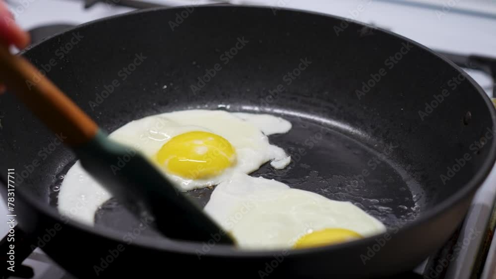 Frying Egg in a Cooking Pan, close-up. Man hands using silicone spatula