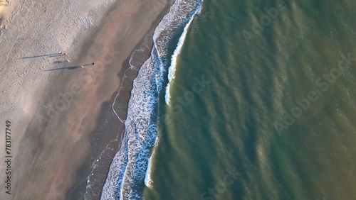 Looking down at people and dogs walking and playing on a quiet beach while gentle ocean waves break into surf in early morning sunlight during a peaceful vacation at Pawleys Island, South Carolina