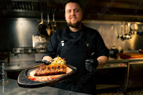 in a professional kitchen the chef stands in his hands with a prepared dish and smiles at the camera