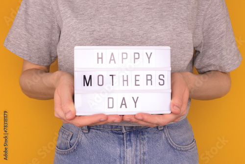 Happy Mothers Day. Female hands hold lightbox with letters in front of yellow background. © rorygezfresh