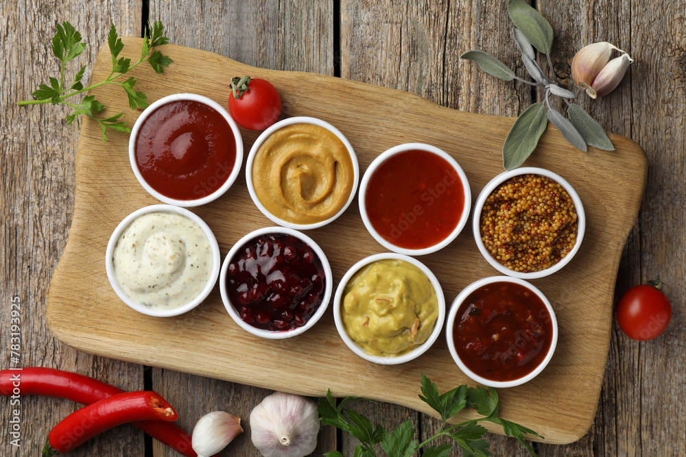 Different tasty sauces in bowls and ingredients on wooden table, top view Different tasty sauces in bowls and ingredients on wooden table, top view