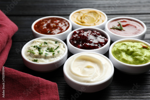 Different tasty sauces in bowls on black wooden table, closeup