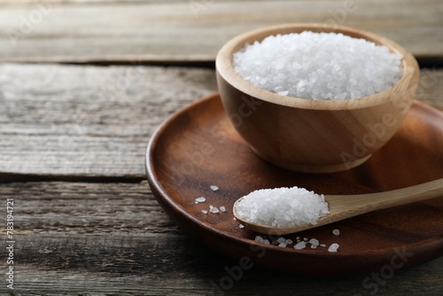 Organic salt in bowl and spoon on wooden table, closeup. Space for text