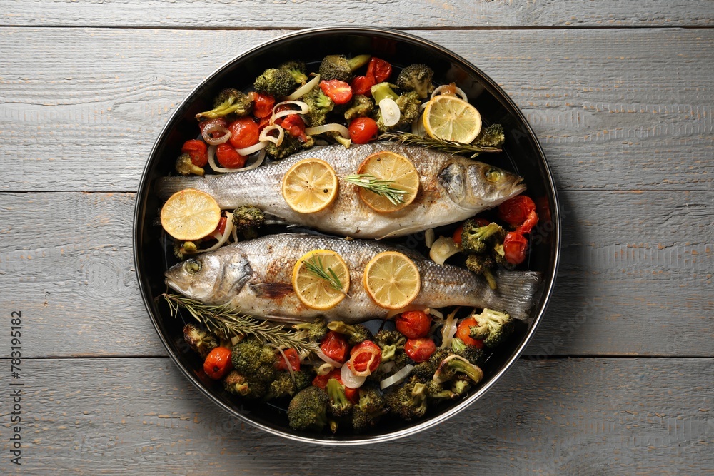 Baked fish with vegetables, rosemary and lemon on grey wooden table, top view