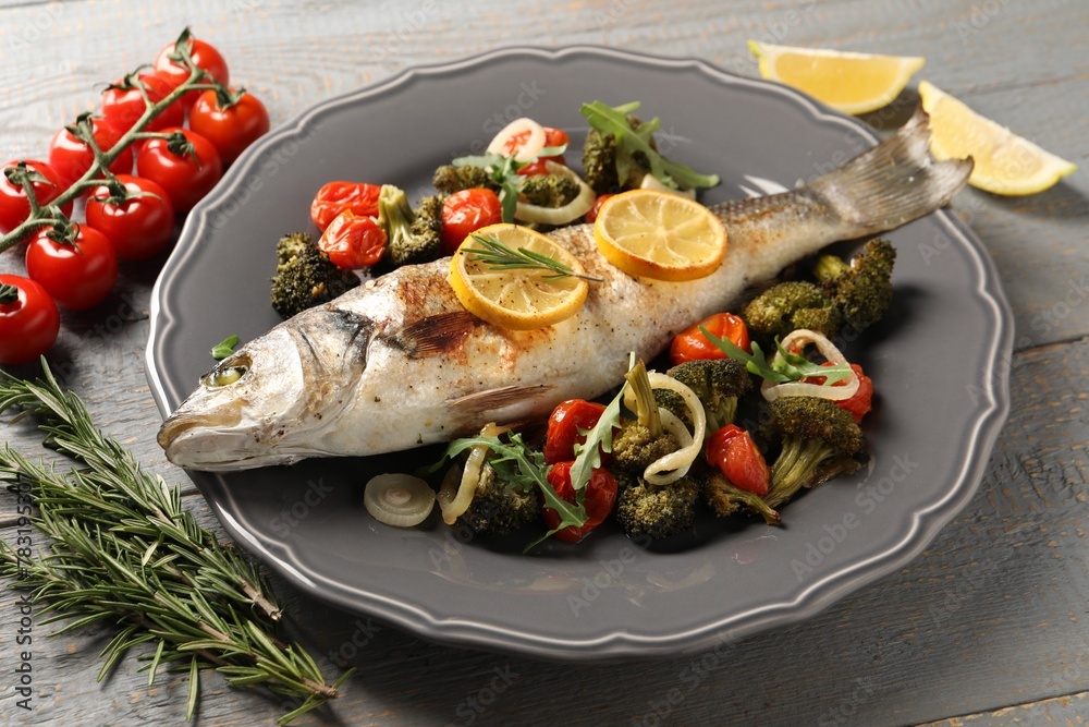 Baked fish with vegetables, rosemary and lemon on grey wooden table, closeup Baked fish with vegetables, rosemary and lemon on grey wooden table, closeup