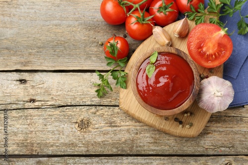Tasty ketchup  fresh tomatoes  parsley and spices on wooden table  flat lay. Space for text