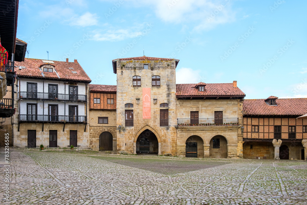 An old building in the medieval town of Santillana del Mar features a prominent clock tower in its center. The architecture showcases historical charm and character.