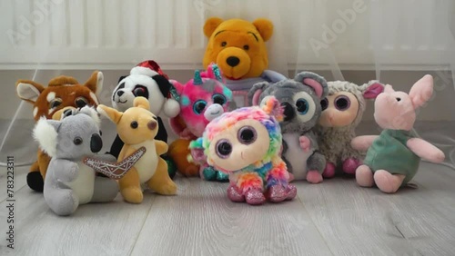 Stuffed and fluffy plush and rainbow toy sheep fall on the laminate flooring in the play area against the backdrop of other toys. Slow motion. photo