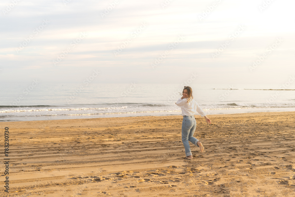 A cheerful woman enjoys a carefree run along the shoreline, feeling the sand between her toes as the sun sets over the ocean