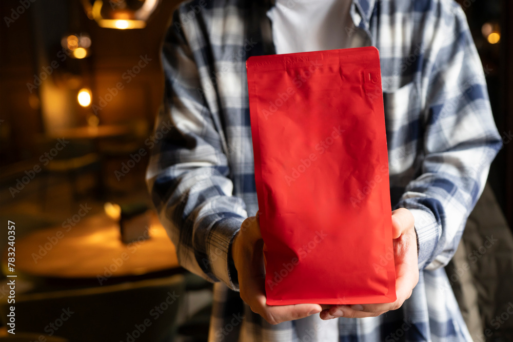 Person Showcasing a Red Coffee Bean Pouch Package in a Coffee Shop, template copy space Person Showcasing a Red Coffee Bean Pouch Package in a Coffee Shop, template copy space