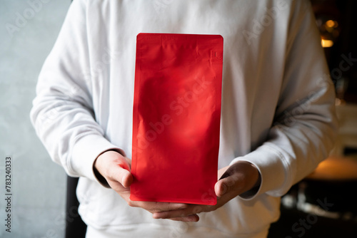 Person Showcasing a Red Coffee Bean Pouch  Package in a Coffee Shop, template copy space