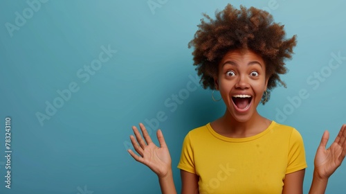 A young African American woman with a fun surprised expression, wearing a yellow shirt against a blue background. Copy space available photo
