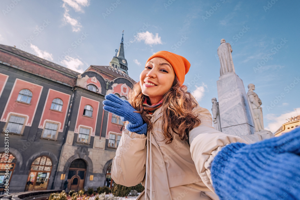 A cheerful young woman explores the charming city of Subotica, Serbia, her vibrant energy adding to the lively ambiance of the historic town hall square.