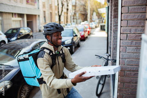 Happy delivery man with a pizza box on a city street photo