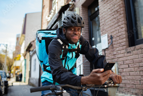 Delivery man on a bicycle wearing a helmet and backpack checking his phone on a city street photo