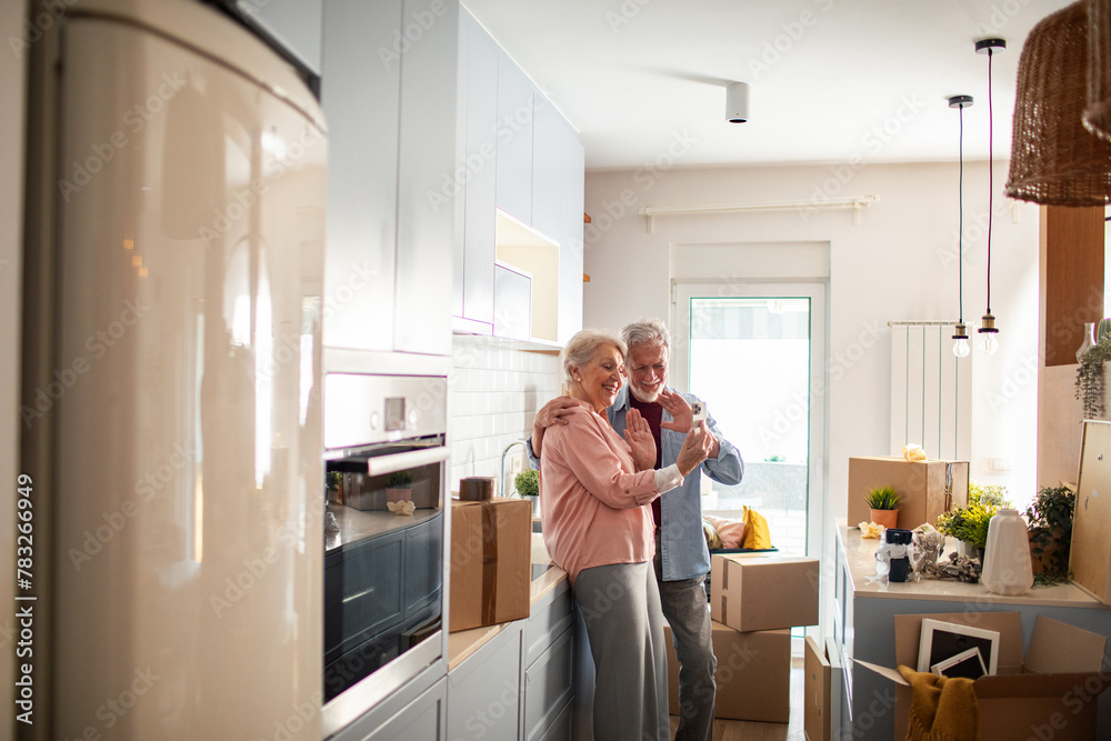 © Marko Geber - Senior couple having video call on smartphone in kitchen with moving boxes © Marko Geber - Senior couple having video call on smartphone in kitchen with moving boxes