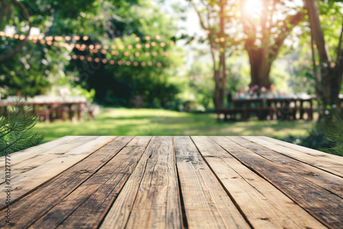 Empty wooden table in summer background with the blurred green garden and party in the background.