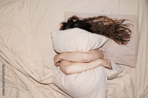 Top view of the persona hiding her face behind pillow in bed. photo