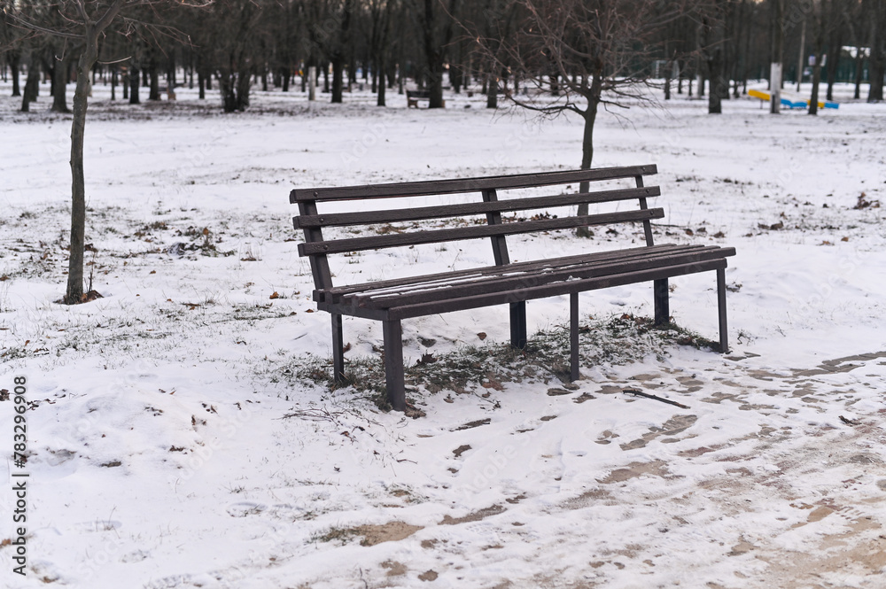 an empty park bench. Snow on the ground