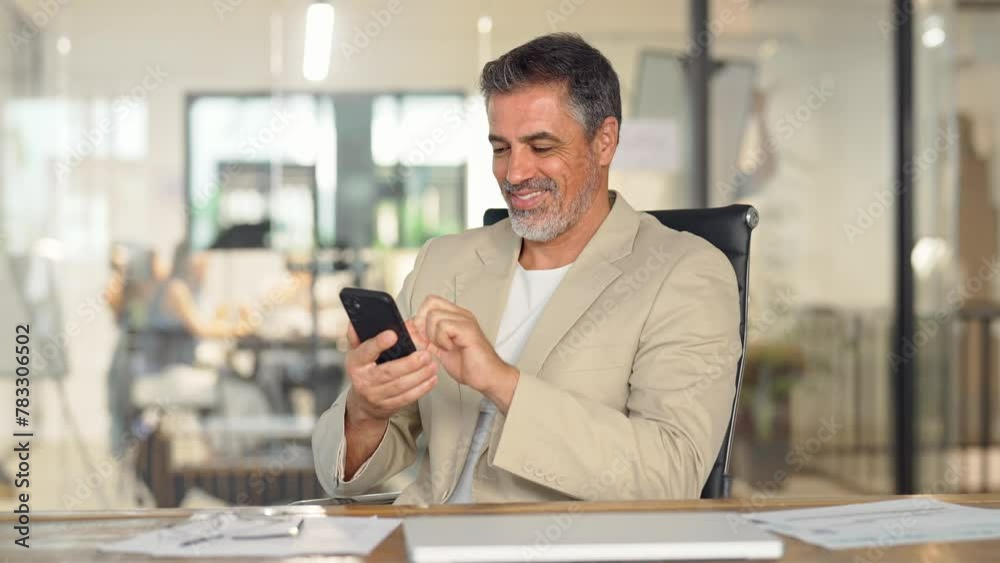 Happy busy middle aged business man ceo investor sitting in office using mobile cell phone. Mature businessman professional entrepreneur looking at smartphone at work making baking payment.