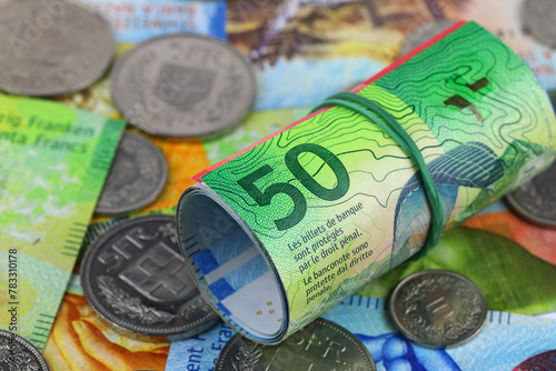 Swiss franc banknotes are rolled up and it lie on the flat other notes and coins, CHF