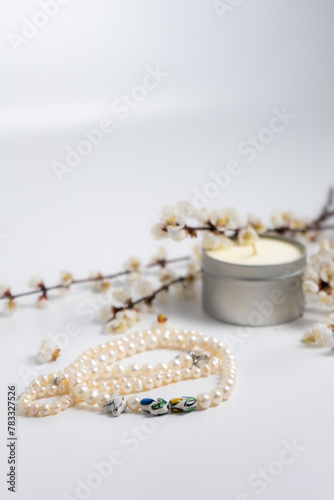 A string of pearls, a candle and blooming branches on white background