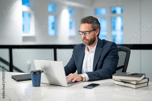 Office workplace. Handsome business man working with laptop at desk in office. Businessman typing on keyboard, online business meeting. Businessman working in office. Office worker using laptop.