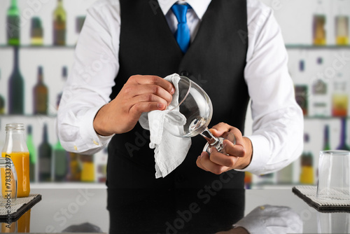Shot of a happy waiter polishing a glass behind the bar photo