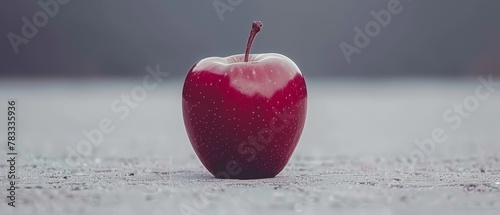   A red apple atop a table, near a black-and-white image of a bitten apple photo