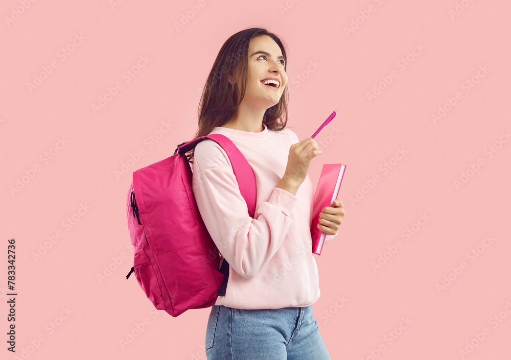 Joyful female student with pen and notebook pondering interesting idea isolated on pink background. Girl in with backpack her shoulders is smiling and looking up and thinking about something. Banner. Joyful female student with pen and notebook pondering interesting idea isolated on pink background. Girl in with backpack her shoulders is smiling and looking up and thinking about something. Banner.