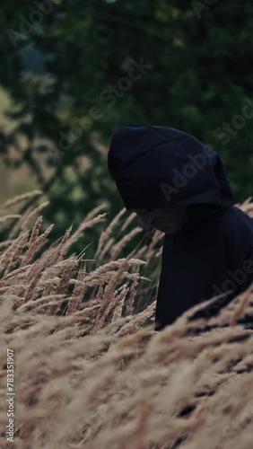 Scary figure with horrorful face outdoors. Ghost in black cloak walking in wheat field. Spooky death among nature. Halloween concept. Vertical video photo