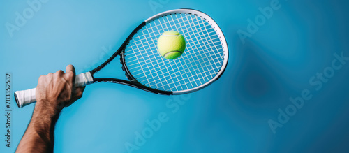 Tennis player is holding racquet and hitting ball on blue background
