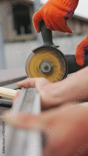 Vertical Screen: Male hand cuts off pieces of pipe with angle grinder. Cutting of a steel with splashes of sparks at construction site. Slow motion of construction worker cutting steel beam