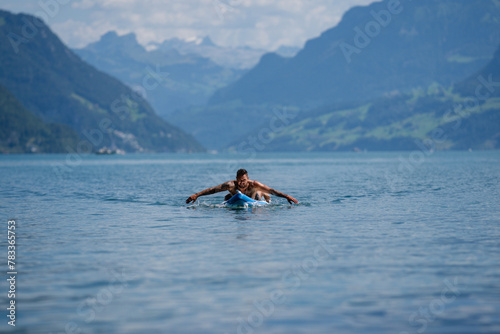 Muscular man with paddle board. Man paddling on paddleboard. Muscular strong Hispanic man on sup board paddle surfing. SUP surfing in summer vacation in Alps lake in Swiss. © Volodymyr