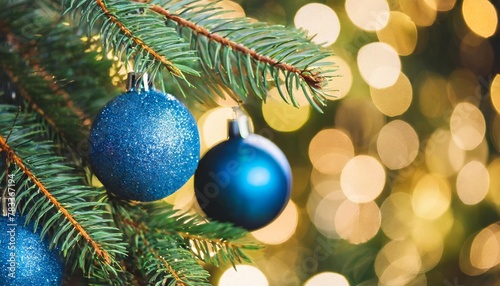 christmas tree with ornaments in blue baubles hanging on fir branches with glittering and bokeh lights in abstract defocused background