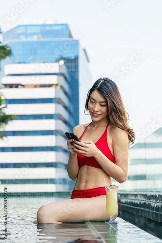 Young woman enjoys sun-kissed serenity, relaxing with drink and using phone in rooftop infinity pool
