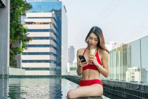 Young woman enjoys sun-kissed serenity, relaxing with drink and using phone in rooftop infinity pool