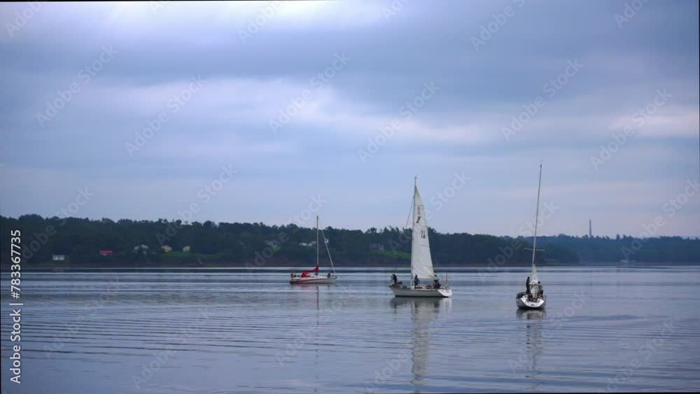 Three sailboats on calm and tranquil water with moody clouds above, as evening approaches Three sailboats on calm and tranquil water with moody clouds above, as evening approaches