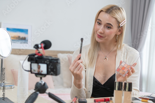 Young woman making beauty and cosmetic tutorial video content for social media. Beauty blogger smiles to camera while showing how to beauty care to audience or followers. Blithe