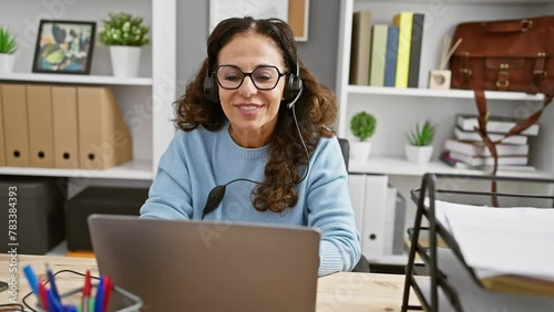 Hispanic woman with curly hair in blue sweater and headset puckering lips in a modern office