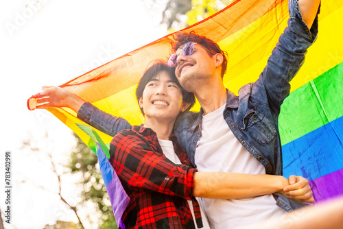 Multi-ethnic gay couple celebrating diversity raising lgbt flag © unai