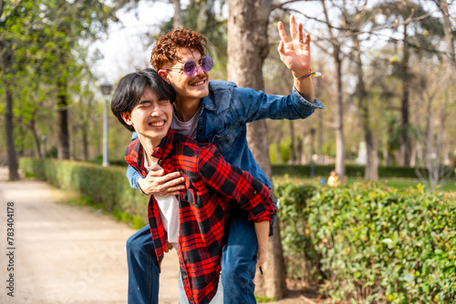 Gay couple having fun in a park waving and piggybacking